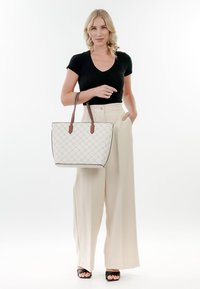 Borsa a tracolla bianca trapuntata con manici in pelle marrone, caratterizzata da un design strutturato e un bordo nero a contrasto, tenuta da una persona con pantaloni chiari.