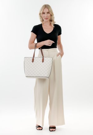 Borsa a tracolla bianca trapuntata con manici in pelle marrone, caratterizzata da un design strutturato e un bordo nero a contrasto, tenuta da una persona con pantaloni chiari.