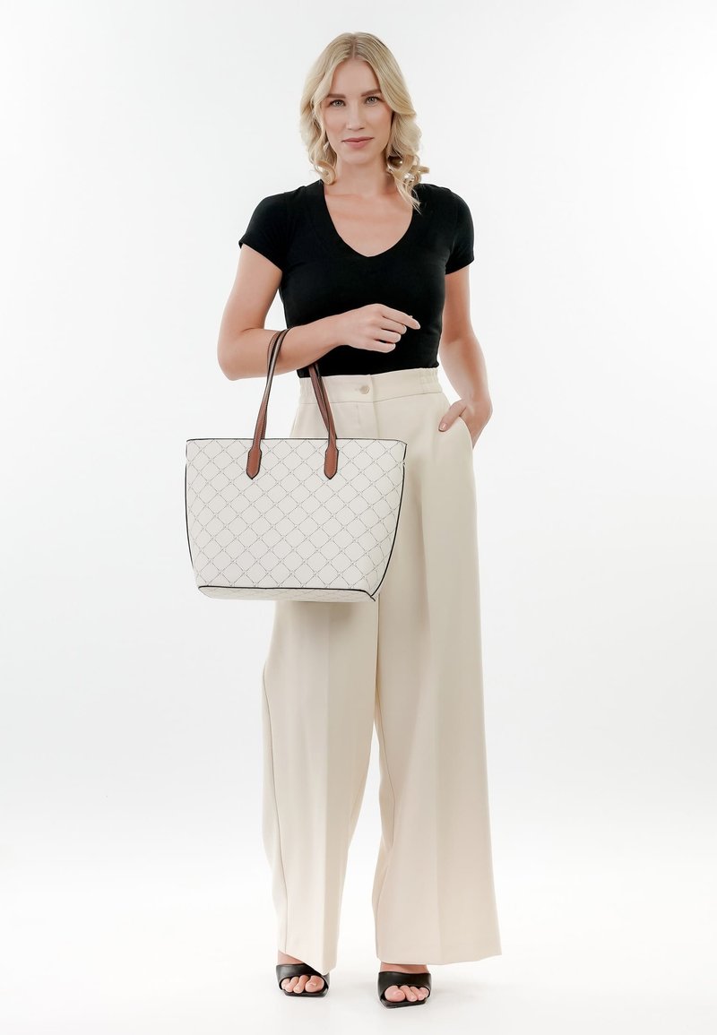 Borsa a tracolla bianca trapuntata con manici in pelle marrone, caratterizzata da un design strutturato e un bordo nero a contrasto, tenuta da una persona con pantaloni chiari.