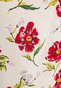 Blomstret stof med en cremet baggrund, der har store røde blomster og mindre hvide blomster, med grønne blade der tilføjer kontrast.