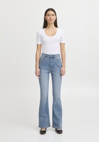 Body a maniche corte bianco abbinato a jeans a vita alta blu a zampa d'elefante, con la classica trama in denim e dettagli di cucitura sottili.