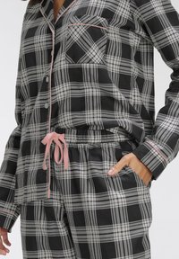 Black and white plaid pajama set with pink accents. Features a button-up top and elastic waistband pants with a drawstring. Soft fabric.