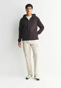 Tume kapuutsiga jakken, millel on ees lukuga, koos heleda beeži värvi kamuflaažipükstega ja valgete tossudega. Sile kude, mugav istuvus.