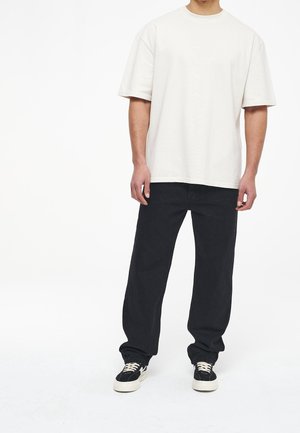 Oversized creme farvet bomulds t-shirt med korte ærmer, parret med afslappede sorte bukser og sorte sneakers med hvid sål og snørebånd.