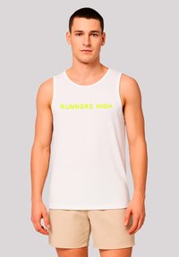 Mann trägt ein weißes ärmelloses Shirt mit gelbem "RUNNERS HIGH"-Text und beigen Shorts, steht vor einem hellgrauen Hintergrund.