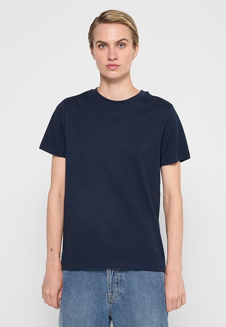 Marineblauwe katoenen t-shirt met korte mouwen, ronde hals en een relaxte pasvorm, gedragen met lichtblauwe denim jeans. Geen zichtbare logo's of patronen.