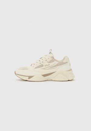 Crème en beige FILA sneaker met mesh panelen, dikke zool en vetersluiting, gezien vanaf de zijkant op een effen achtergrond.