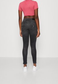 Jeans ajustados negros de cintura alta, con bolsillos traseros y detalles en costura blanca. Combinados con una camiseta corta rosa y zapatillas blancas.