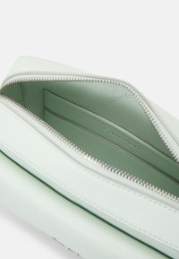 Ljusgrön läderkuvert med dragkedjestängning. Inuti finns kortfickor och en slät yta; Calvin Klein-logotyp präglad inuti.