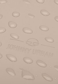 Suprafață roz deschis cu picături proeminente și un logo embosat "JOHNNY URBAN". Textură netedă, design minimalist, estetică modernă.