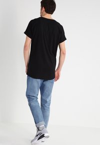 Camiseta negra de manga corta combinada con jeans de mezclilla azul claro. Los jeans están ligeramente doblados en los puños, y el conjunto incluye zapatillas grises.