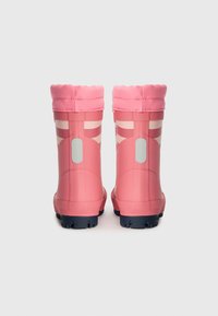 Botas de goma rosas con una banda superior en forma de onda, que presentan rayas blancas y una suela de color azul marino, vistas desde atrás sobre un fondo liso.