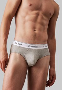 Grå bomullsunderbukse med hvit elastisk midje som har trykt "Calvin Klein"-logo. Figurtilpasset design med en glatt tekstur.