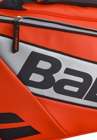 Orange taske med en struktureret overflade, sorte detaljer og et stort sølvlogo. Inkluderer en lynlåscompartiment med en mærket trækstang.