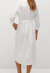 Weißes Hemdblusenkleid mit langen Ärmeln, tailliertem Gürtel, strukturierter Rückseite und Falten. Aus glattem Stoff mit klassischem Kragen gefertigt.