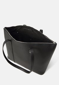 Svart lær tote-bag med glidelås, eksteriør-logo og to hanke. Innvendig har den et enkelt fôr med en glidelåslomme.