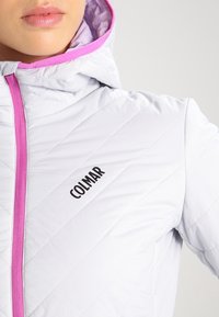 Giacca isolata grigia chiara con zip e cappuccio rosa, caratterizzata da un design a rombi e un logo nero sul lato sinistro del petto.