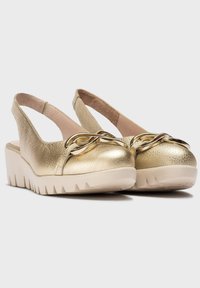 Zapatos slingback de cuero dorado con parte superior texturizada, que presentan un acento metálico y una suela de plataforma blanca gruesa con fondo con relieve.
