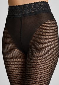 Hooggepaste zwarte kanten panty met bloemenband en geometrisch gaaspatroon dat de benen en heupen bedekt.