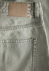 Jeans de denim gris claro con una textura suave, que cuentan con una etiqueta cuadrada de cuero marrón y costuras en contraste en la cintura y el bolsillo.