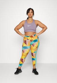 Top desportivo roxo, com um logótipo branco, combinado com leggings vibrantes que apresentam um padrão geométrico em tons de amarelo, azul e rosa.