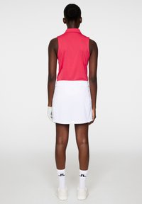 Rosa ärmlös polo med krage, kombinerad med en vit kjol. Har vita detaljer och en handske. Stående figur sedd bakifrån.