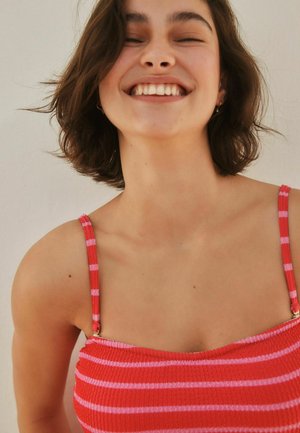 Raudonos ir rožinės spalvos dryžuotas susmaugtas viršus su plonomis petnešėlėmis, pagamintas iš tekstūruotos medžiagos ir dekoruotas aukso spalvos detalėmis.