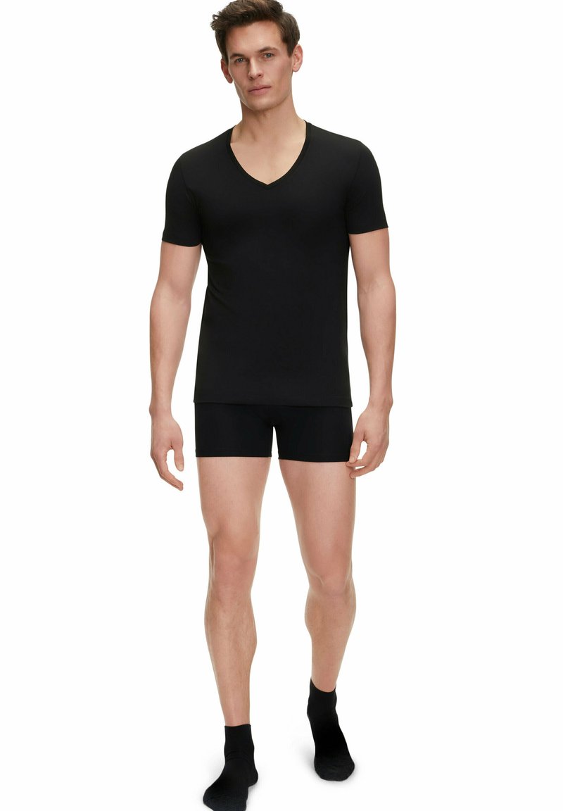 Schwarzes kurzärmeliges V-Ausschnitt-T-Shirt kombiniert mit schwarzen, engen Shorts. Glatte Textur; simples Design; Standardlänge. Schwarze Knöchelsocken.