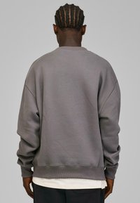 Grå oversized sweatshirt med rund hals, senket skuldre, ribbede mansjetter og kant. Myk tekstur og minimalistisk design.