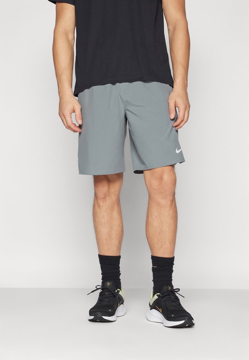 Graue Sportshorts mit elastischem Bund, kombiniert mit schwarzen Sneakers und schwarzen Kniestrümpfen. Die Shorts haben ein kleines weißes Logo.
