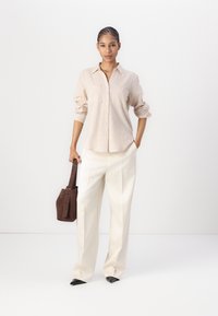 Light beige button-up shirt with rolled sleeves, white wide-leg trousers, black pointed-toe shoes, and brown handbag with a short handle.