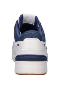 Witte sneaker met een marineblauwe mesh bovenkant en leren accenten. Kenmerkt zich door een gevoerde kraag, rubberen zool en een gemodelleerde tussenzool met blauwe details.