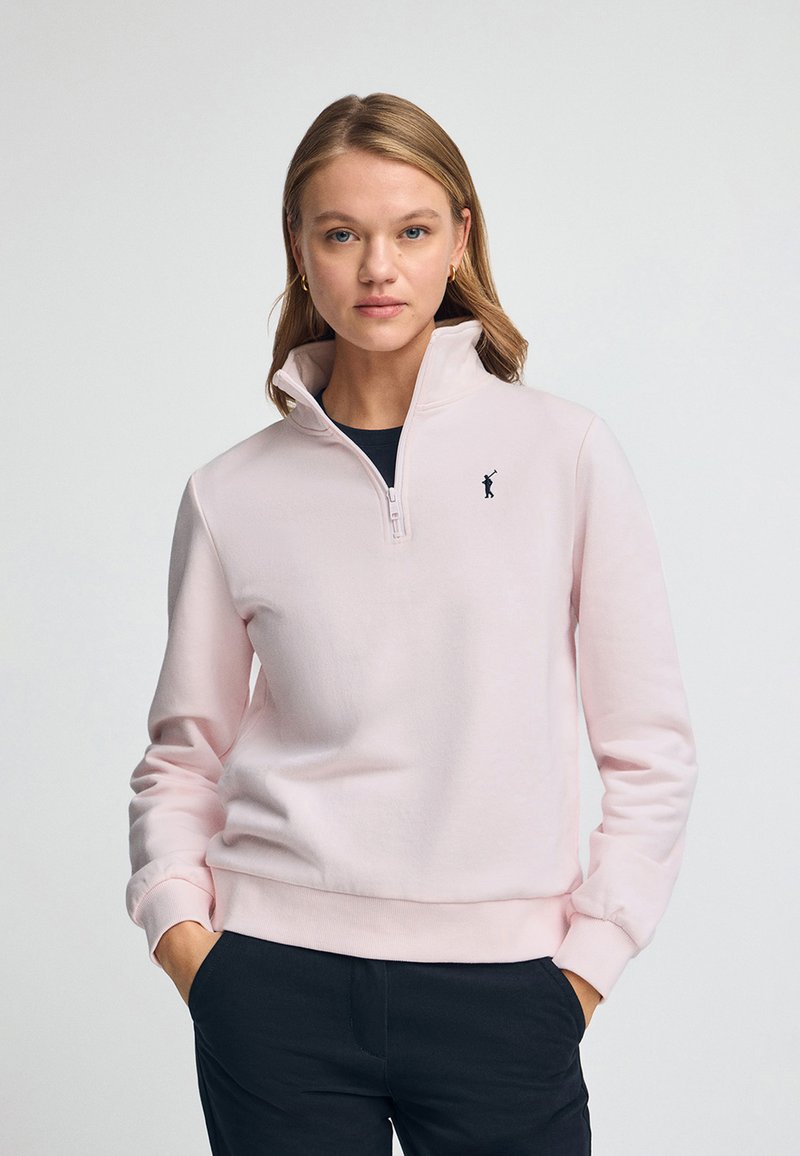 Ljusrosa zip-up sweatshirt med hög krage, mjukt tyg, ribbade ärmslut och en liten svart logotyp på vänster bröst.