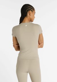 Top sportivo beige a costine con maniche corte e design aderente. Un piccolo logo è visibile sulla parte superiore della schiena. Il tessuto appare liscio.