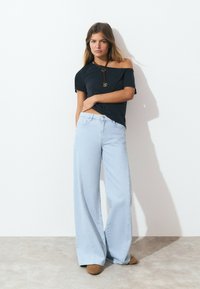 Light blue wide-leg jeans with a high waist and light wash fabric, paired with a black off-the-shoulder top and brown suede shoes.
