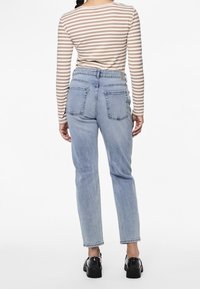 Jeans de tiro alto en azul claro con un corte recto, que cuentan con dos bolsillos traseros y una textura ligeramente descolorida. Combinados con una blusa a rayas.
