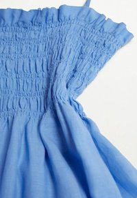 Tissu bleu clair avec un design smocké, comprenant de délicates plissures et des bords froncés. Texture douce, adaptée à une tenue décontractée.