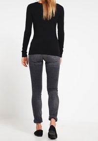 Musta pitkähihainen istuva paita, joka on yhdistetty harmaisiin kapeisiin farkkuihin, joissa on käännetyt hihansuut ja mustat nilkkurit. Sileä pinta ja yksinkertainen muotoilu.