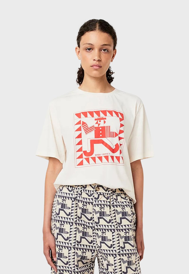 Krémové tričko s krátkým rukávem s červenou a bílou geometrickou grafikou, doplněné vzorovanými kalhotami s modrashými a krémovými designovými prvky.