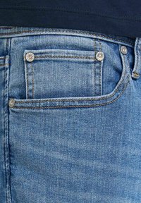 Ljusblå denimjeans med en liten myntficka som har mässingsnitar, synlig sömnad och en slät yta.