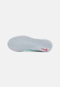 Futballcipő talpa világosszürke gumiból készült, textúrázott mintával és piros Nike logóval kiegészítve. Ívelt formát kínál a tapadás érdekében.