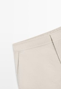 Short beige avec une taille élastique et des poches latérales, posé à plat sur un fond blanc.