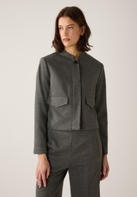 Graue, kurze Jacke aus strukturiertem Stoff mit vertikalen Streifen, ausgestattet mit einem hohen Kragen, Knopfleiste und zwei Fronttaschen.