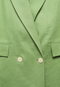Blazer verde in lino con rever a punta, design doppiopetto e due bottoni color crema. Include due tasche frontali.