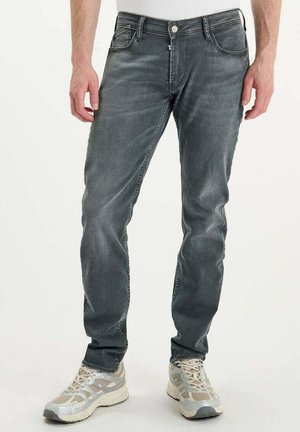 Jean en denim gris avec une coupe slim, cinq poches et une légère décoloration. Associé à des chaussures de sport gris clair avec des détails en mesh.