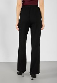 Black wide-leg pants made from textured fabric, featuring a flat waistband and a relaxed fit. Suitable for casual or formal occasions.