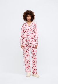 Conjunto de pijama rosa com padrão de fita vermelha, apresentando uma camisa de botão de mangas longas e calças retas combinando, feito de tecido suave.