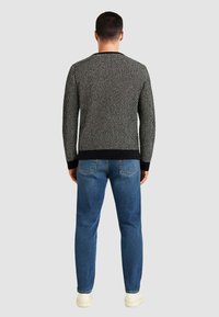 Maglione nero e bianco lavorato a maglia con motivo strutturato, polsini e orlo a costine blu navy, abbinato a jeans blu e sneakers bianche.
