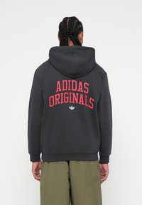 Tmavomodrý mikina s kapucňou, na zadnej strane so silným červeným textom "ADIDAS ORIGINALS" a elastickými manžetami. Mäkká tkanina s hladkým povrchom.