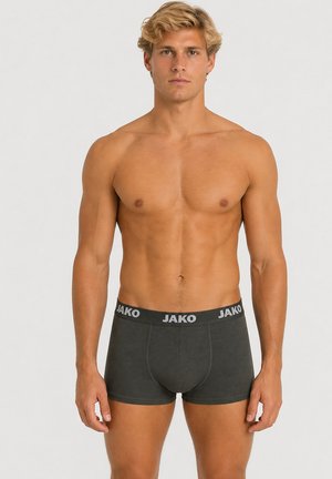 Blonder Mann mit muskulösem Körperbau, der dunkelgraue JAKO Boxershorts trägt, steht vor einem schlichten hellgrauen Hintergrund.